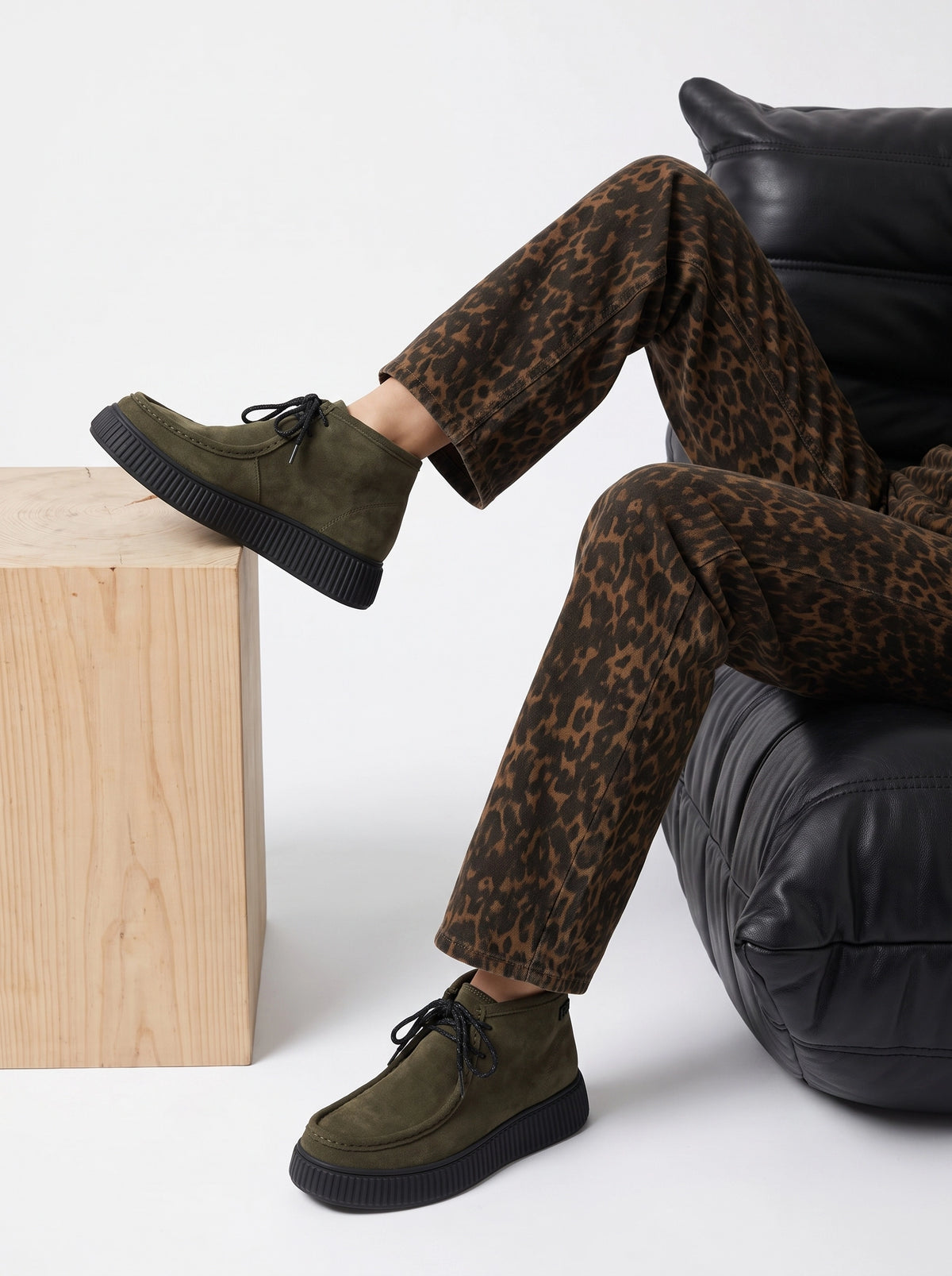 Derbies Piper kaki portées avec un pantalon imprimé léopard, assise dans un fauteuil en cuir noir.