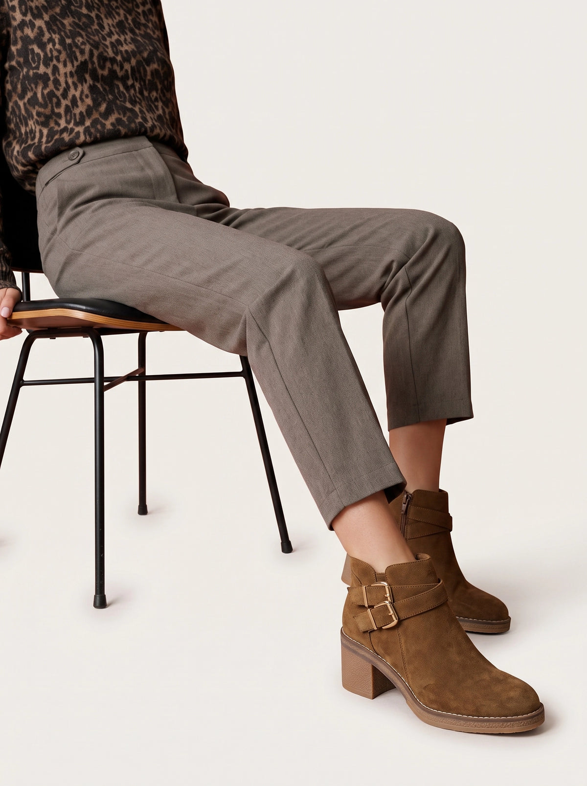 Bottines Parina camel portées avec un pull imprimé léopard et un pantalon gris, assise sur une chaise.