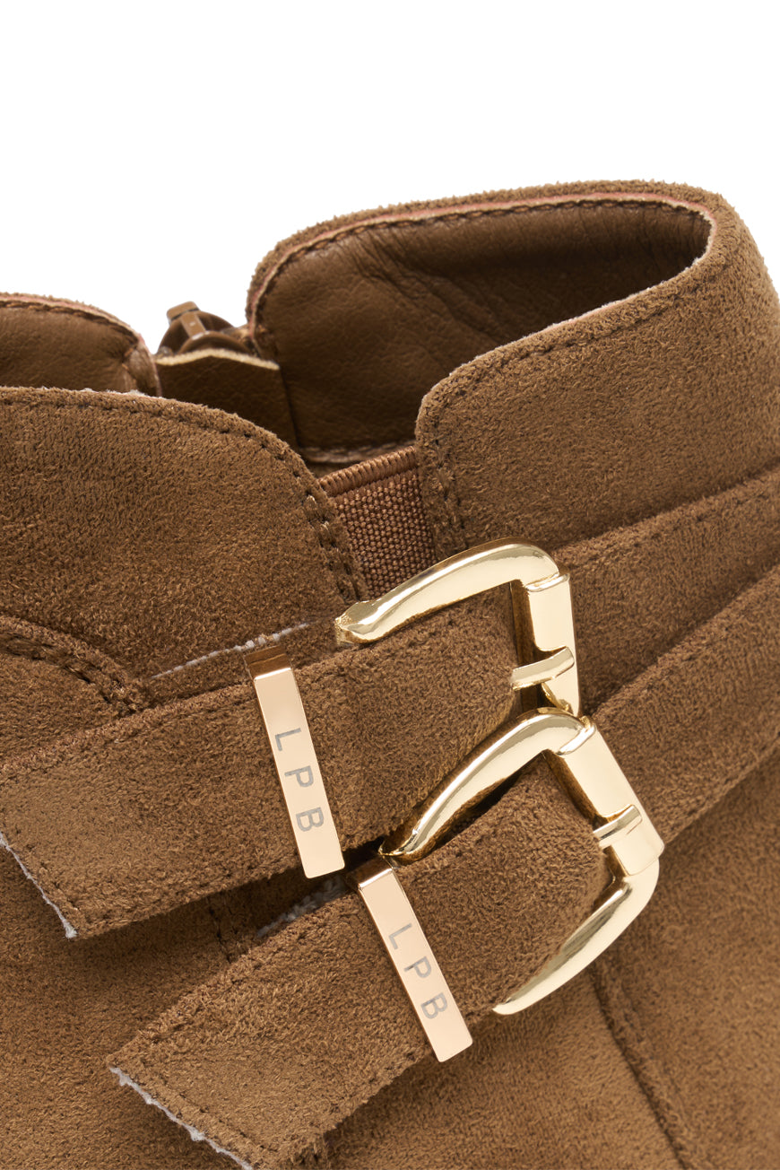 Bottines Parina camel portées avec un pantalon gris, assise sur un tabouret.