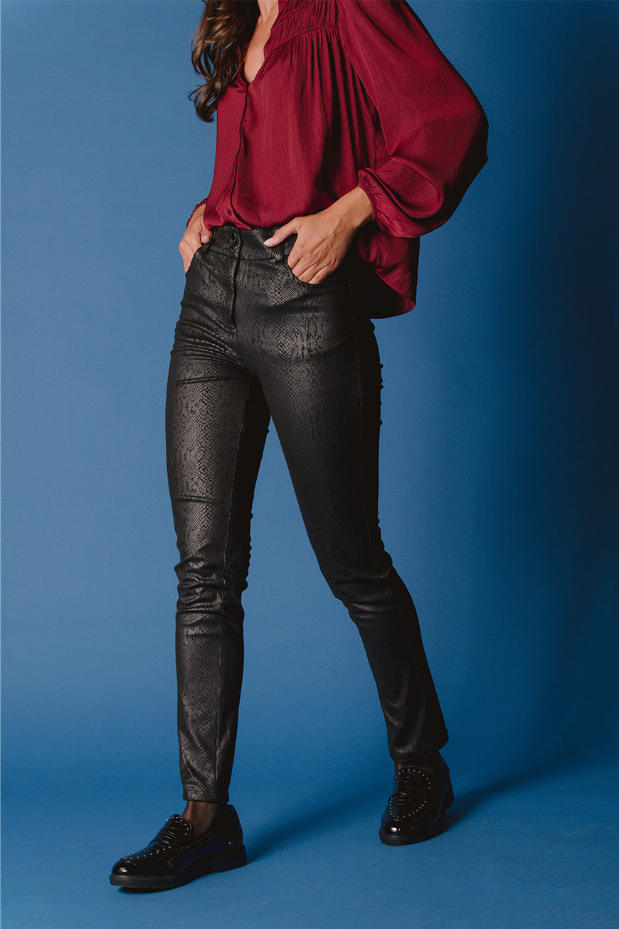 Pantalon Penina noir imprimé python skinny, porté avec un chemisier bordeaux et des mocassins noirs.