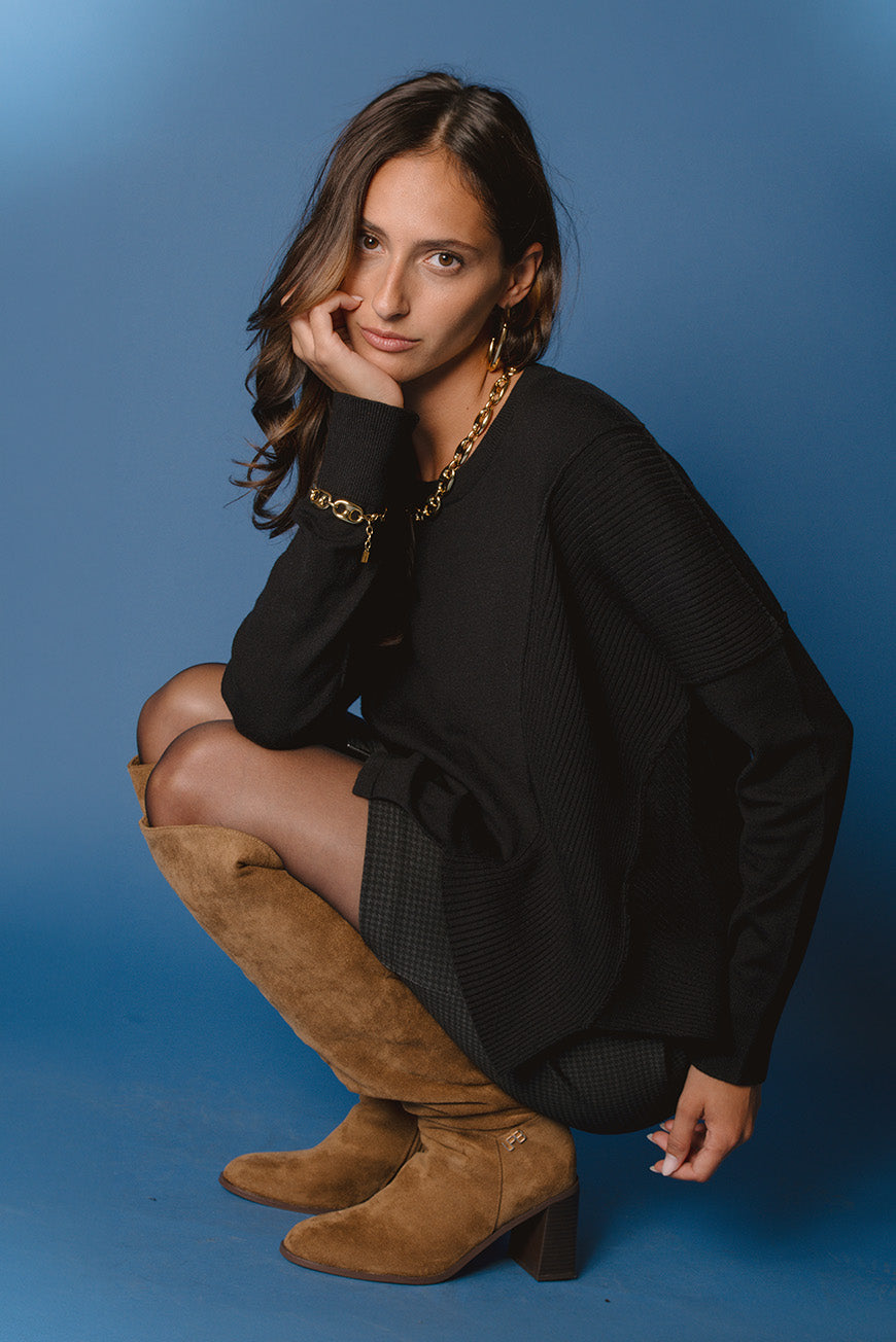 Pull Pamina noir à empiècement côtelé, porté accroupi avec des bottes en daim camel.