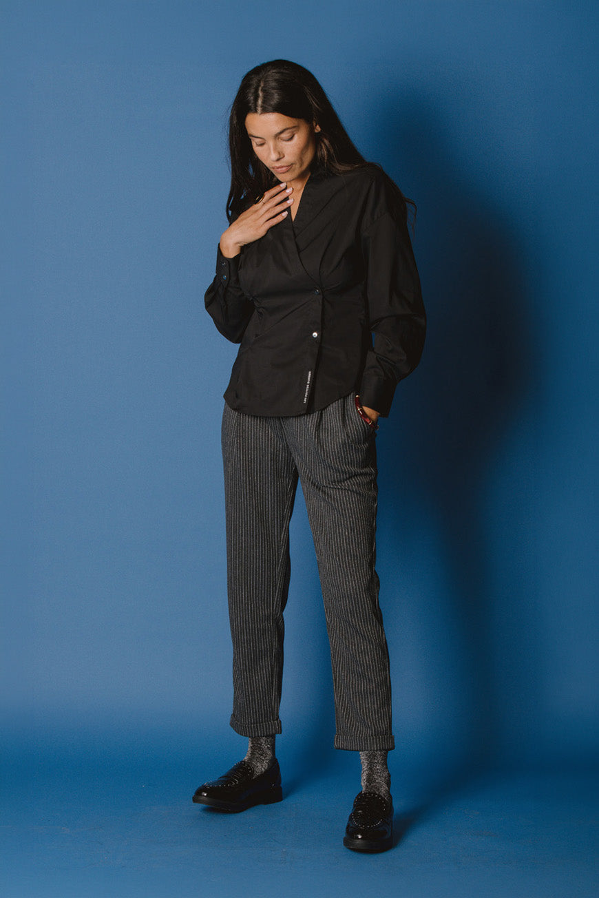 Pantalon Cassendra rayures brillantes gris à revers, porté avec une chemise noire croisée.