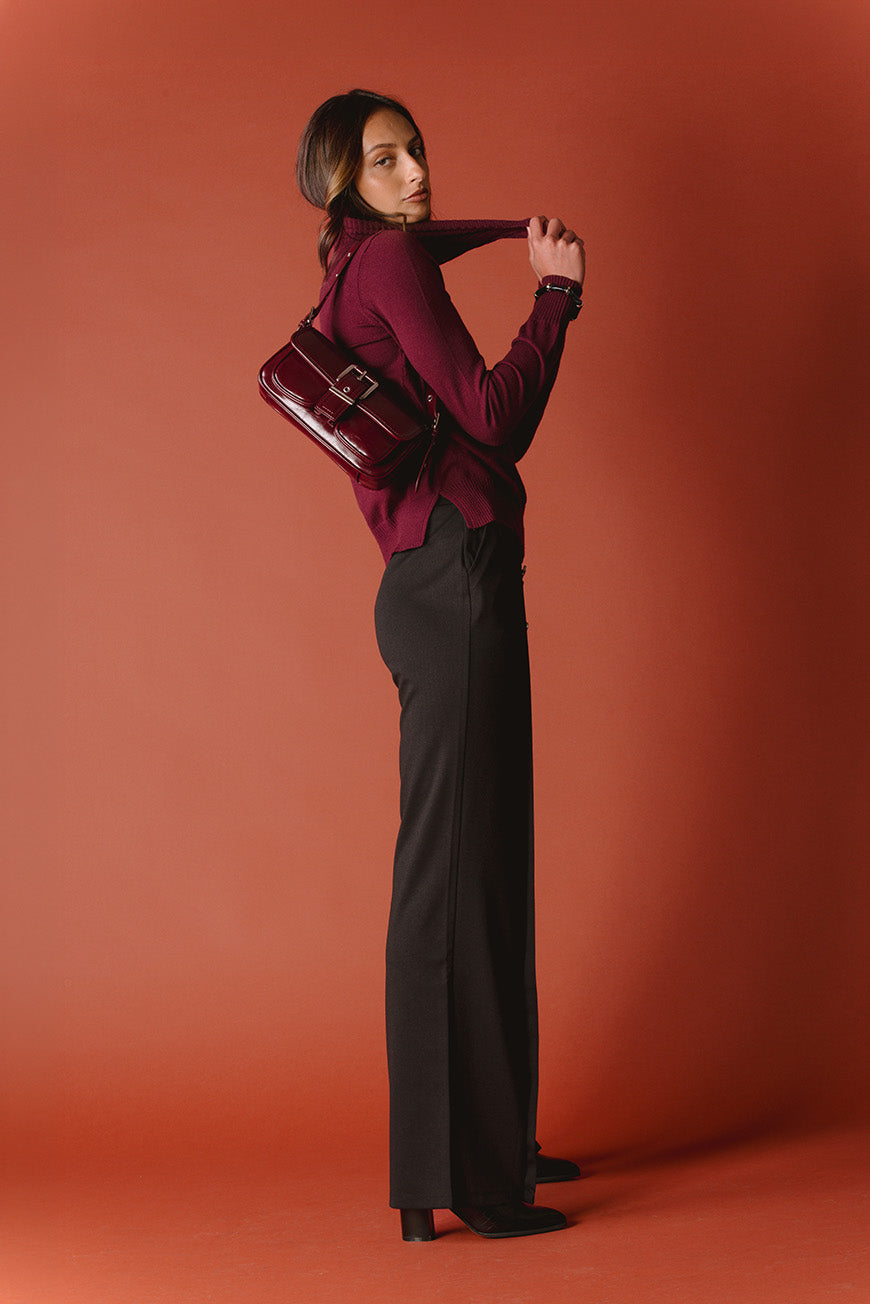 Pantalon Pharailde noir large, porté avec un sac bandoulière bordeaux verni et un pull bordeaux.