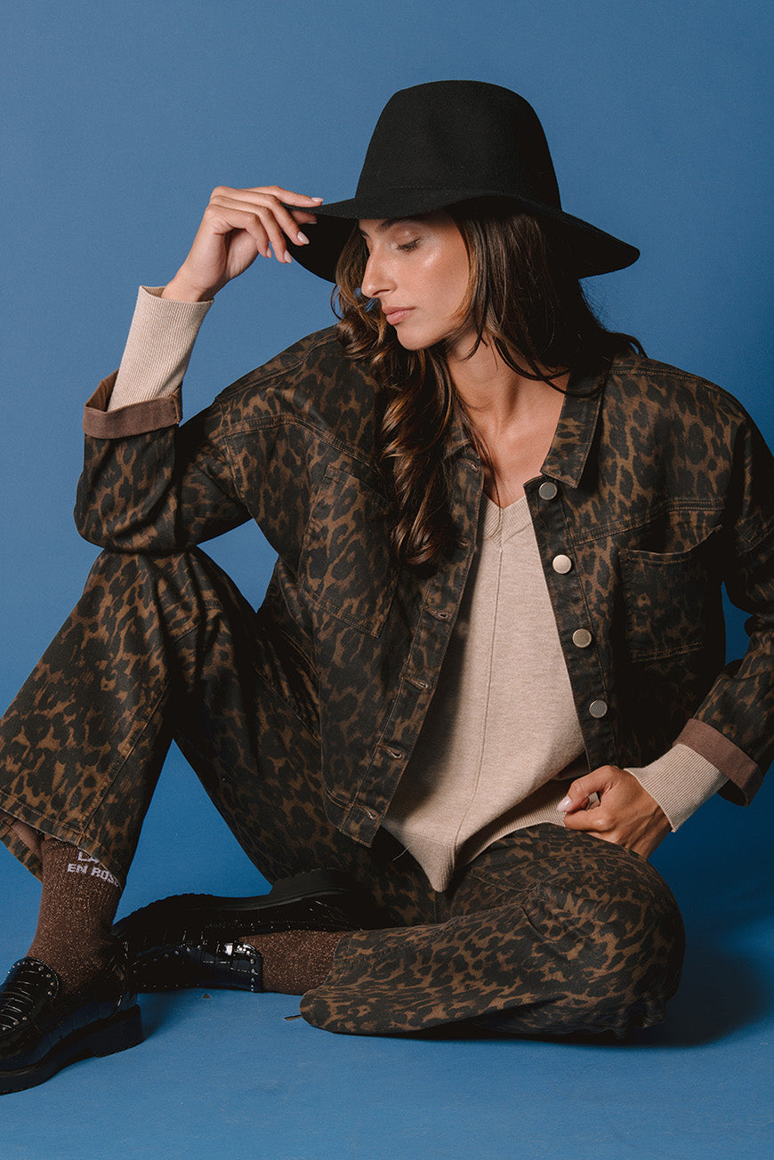 Veste Pamela imprimé léopard assise, portée avec un pantalon assorti et un chapeau noir.
