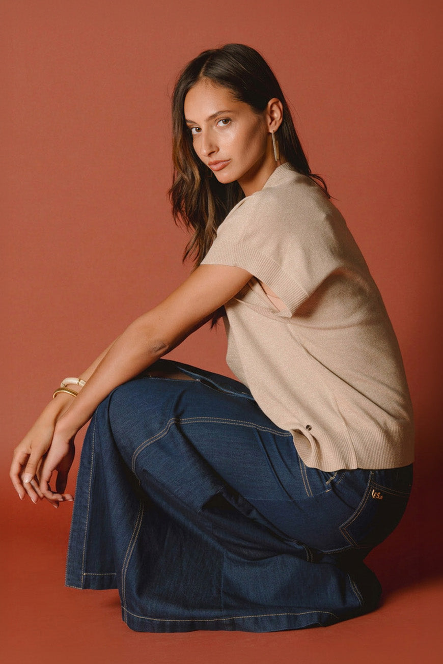 Jupe Prissie longue en jean brut, portée assise avec un pull beige asymétrique.