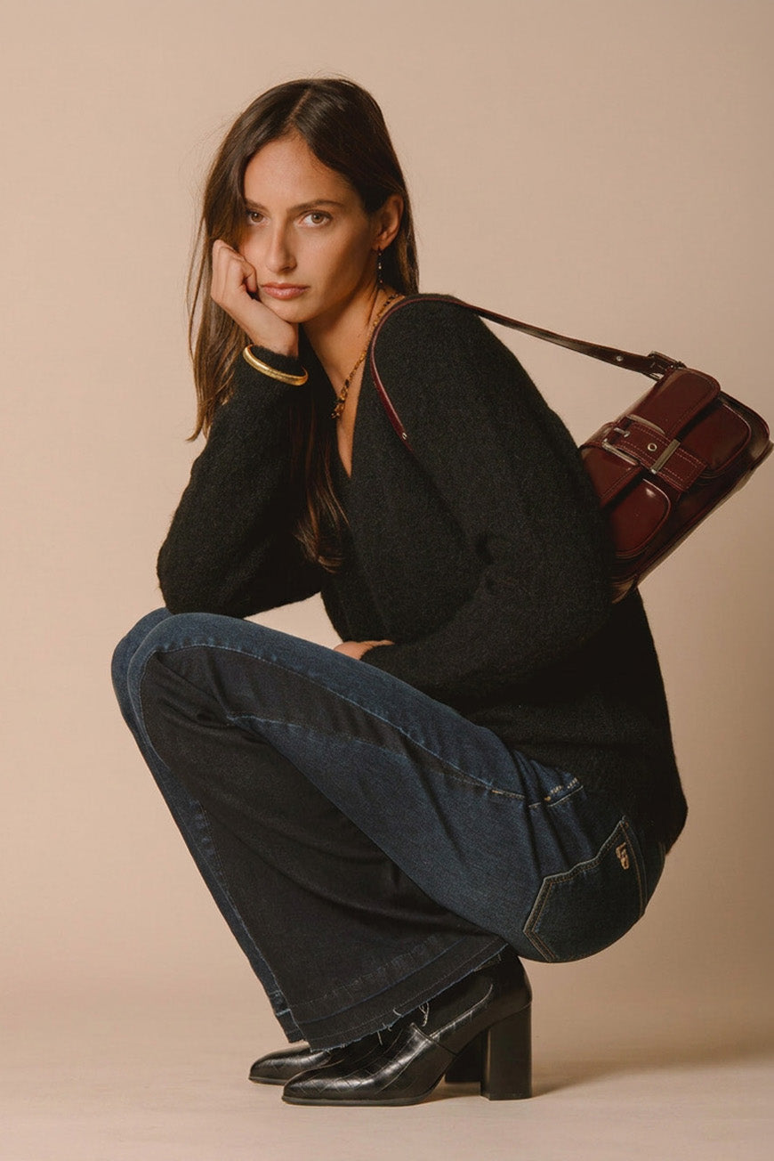 Pull Jamelia noir col V, porté accroupi avec un sac bordeaux en bandoulière