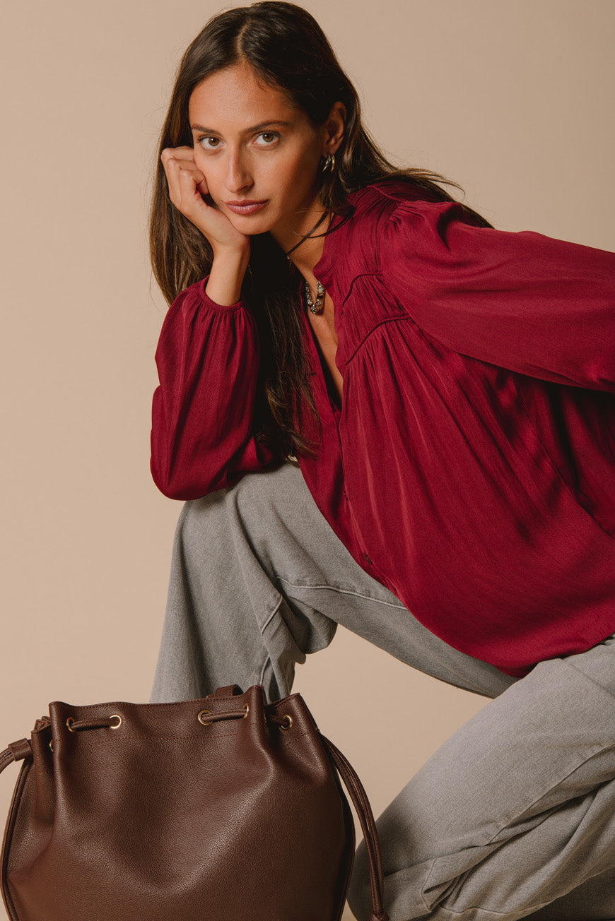 Blouse Palmina bordeaux en satin, portée assise avec un sac en cuir marron
